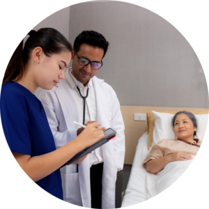 A student wearing blue scrubs holds and iPad while a person in a white lab coat stands behind her. In the background there is a woman laying on a hospital bed.