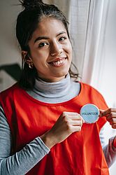 A girl in an orange vest smiling, holding a volunteer pin