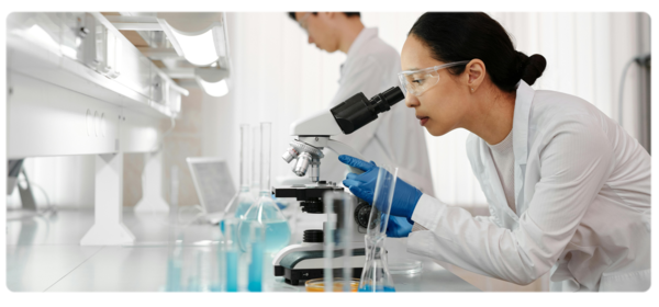A biochemist looks through a microscope in a bright white lab environment