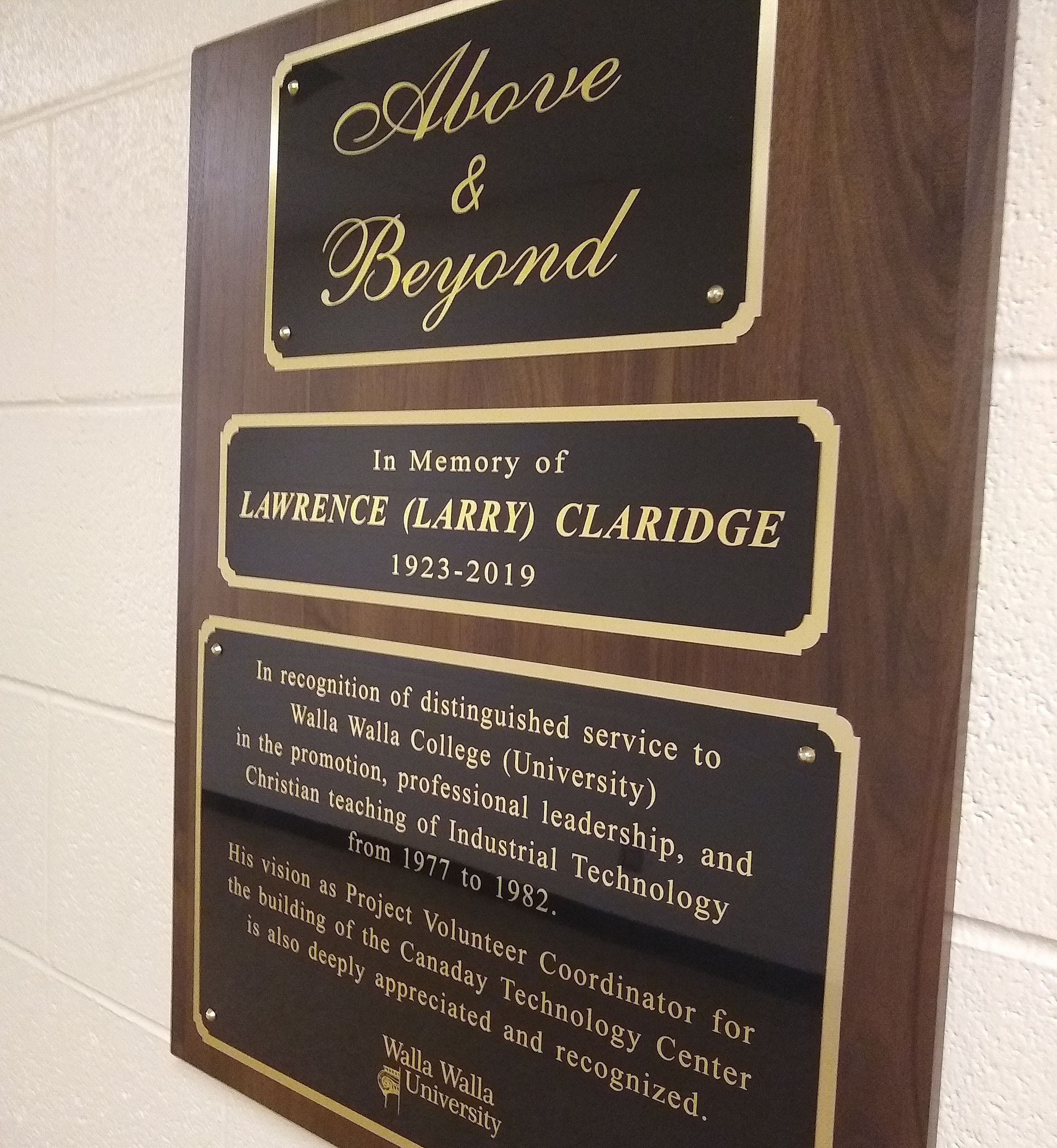 Black and wooden plaque with gold writing hanging on white wall.