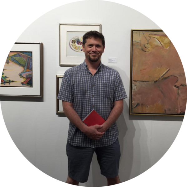 A man stands between several paintings in an art gallery.