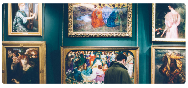 Student standing in front of a wall of paintings in a gallery