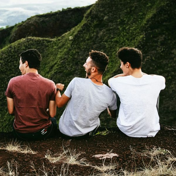 Three young men sitting and talking facing mountains