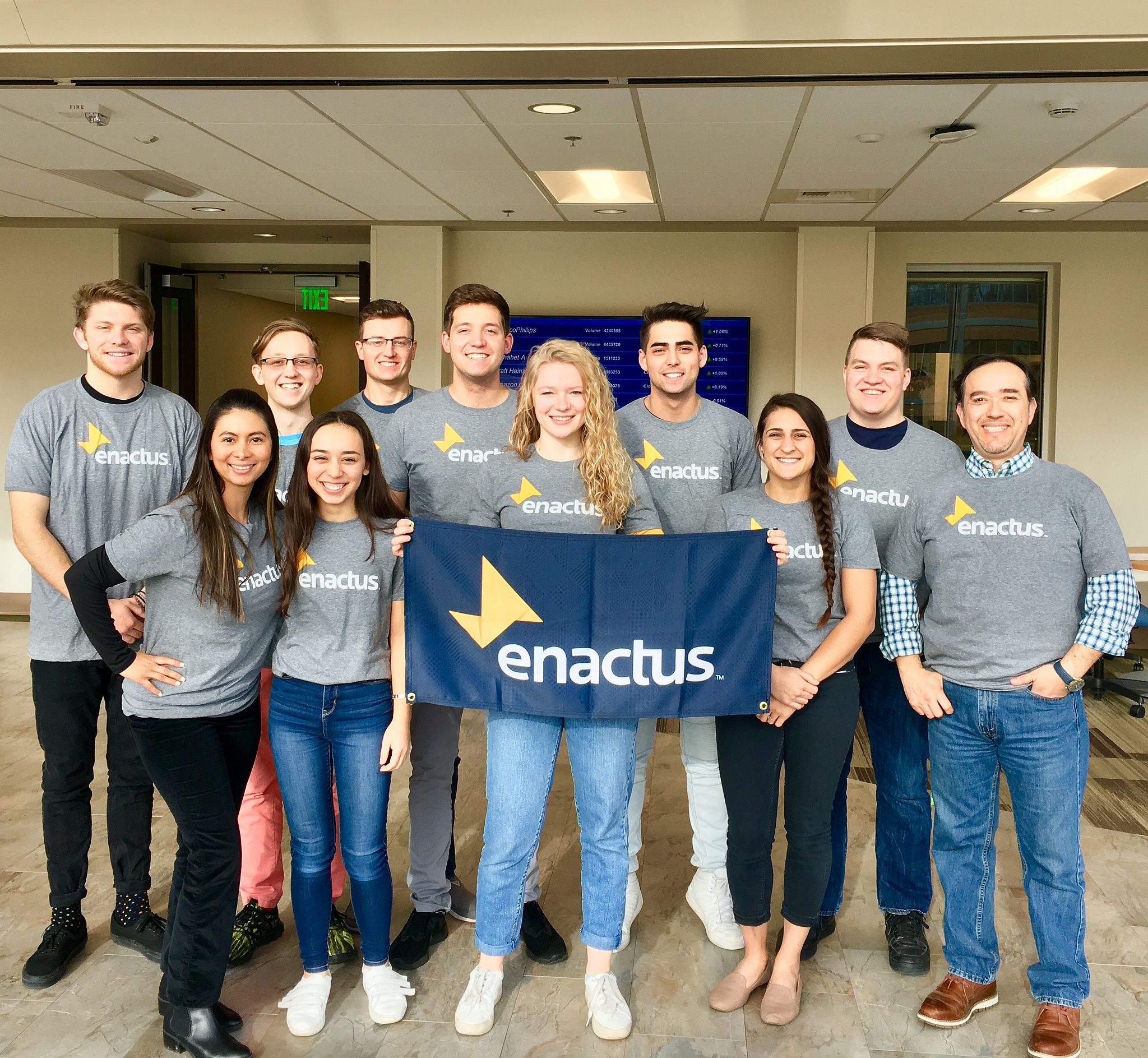 Enactus team standing in matching gray shirts with the enactus logo and holding an enactus banner.