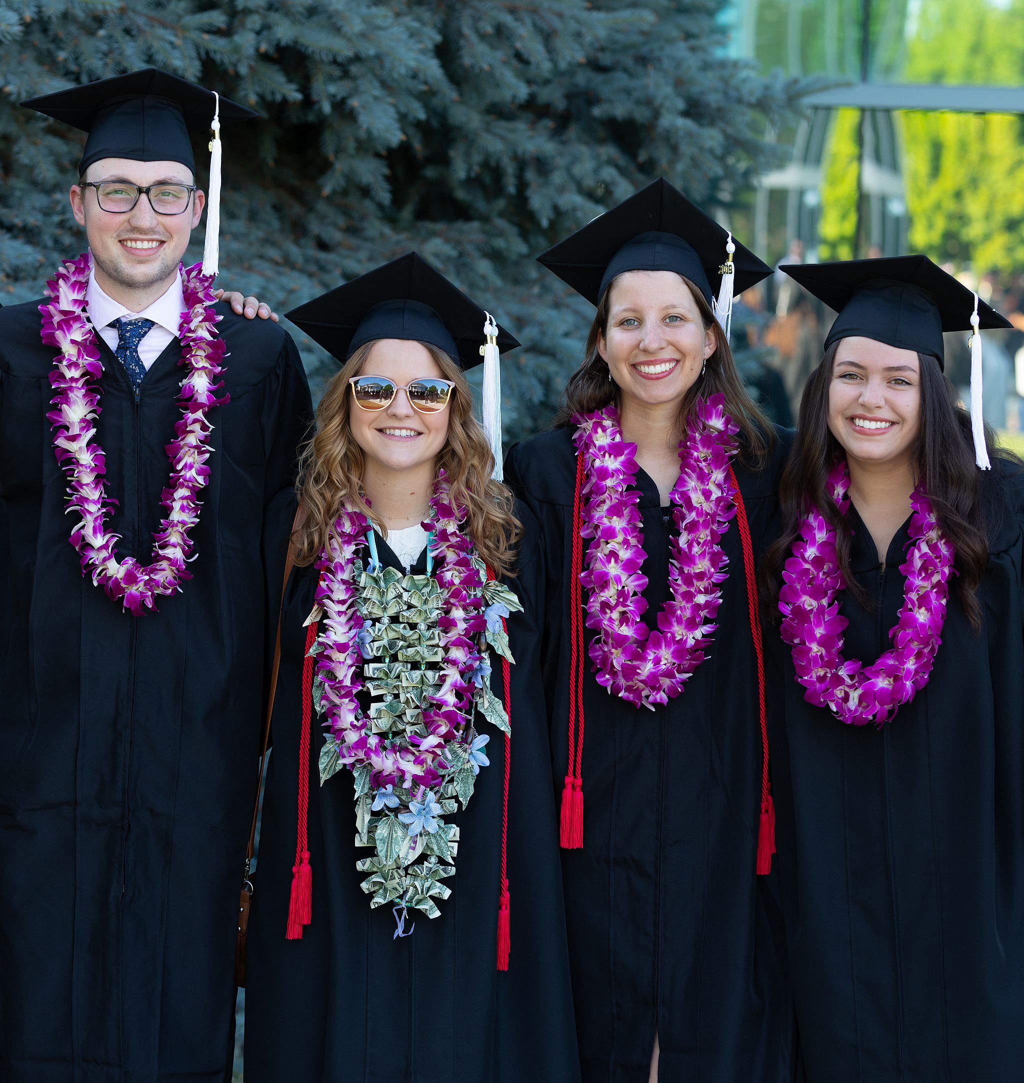 Four graduates in caps and gowns pose in a row, one man and three women.