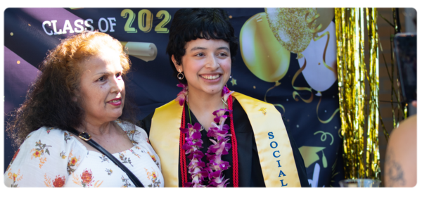 A graduating Social Work student stands with a parent in front of a Photo Booth backdrop