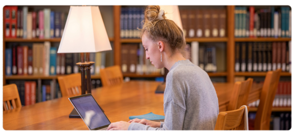 A student works at a laptop at a table in the Peterson Memorial Library.