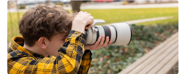 A student holds a camera and takes photos of something in the distance.