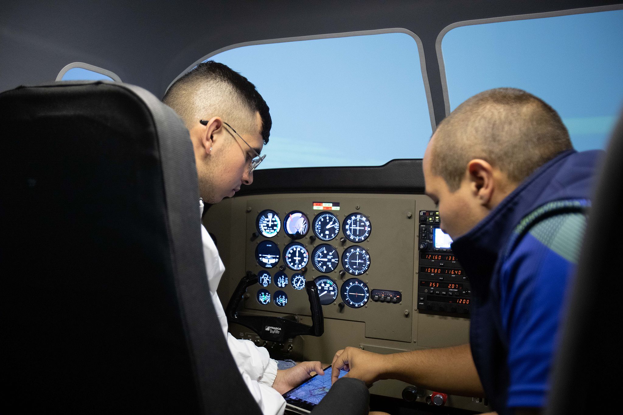 Instructor points out details on a map to student in an airplane cockpit.
