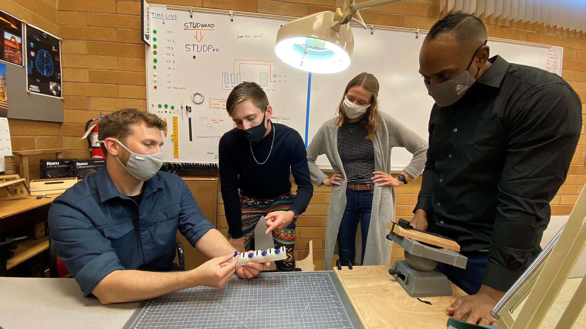 A team of four students wearing masks gather to evaluate their project.
