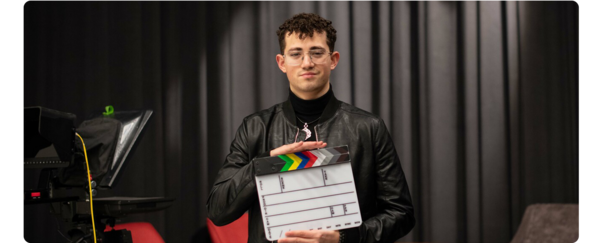 A student standing on a film set holding a clapper board.