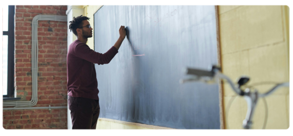 Person stands at blackboard and writes with chalk