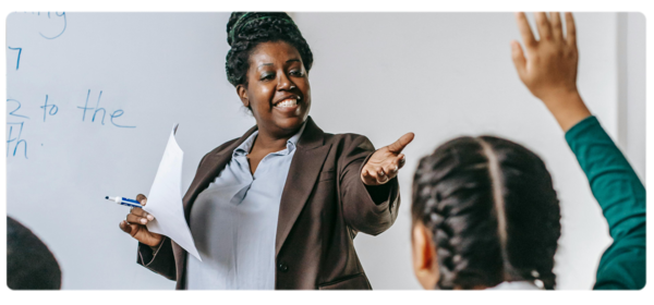 Smiling teacher motions to child with raised hand