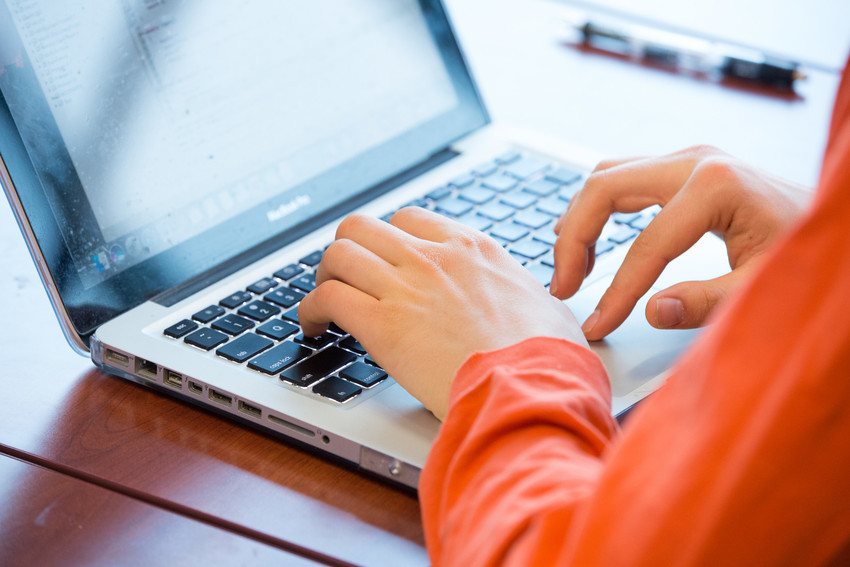 student's hands and arms typing on a laptop keyboard