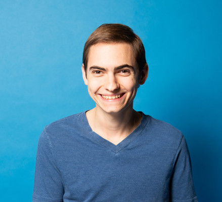 young man in a blue shirt smiling against a blue background.