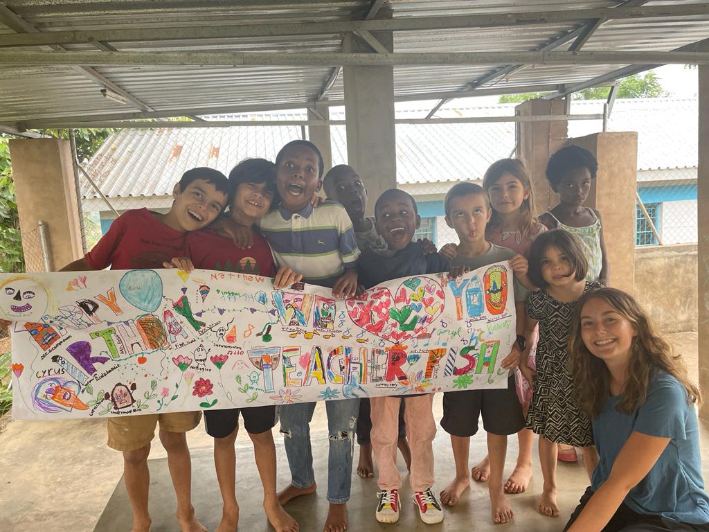 Madelyn and her students hold a hand-drawn sign.